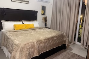 Un dormitorio con cama, cabecera, mesita de noche, lámpara, ventana con cortinas y vista al exterior.