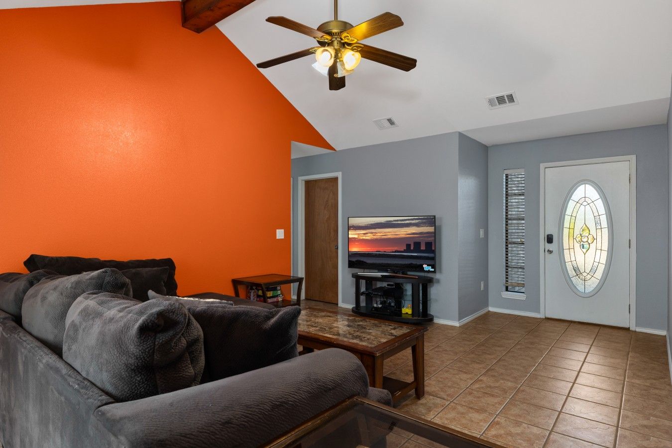 A living room with a sectional sofa, a television, a ceiling fan, and a door with a stained glass window.