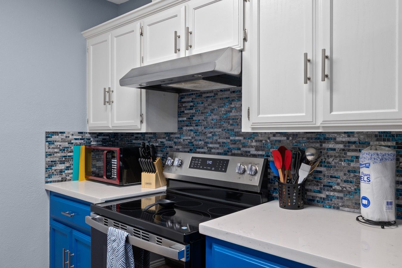 A kitchen with white cabinets, a black stove, a microwave, and a tiled backsplash.