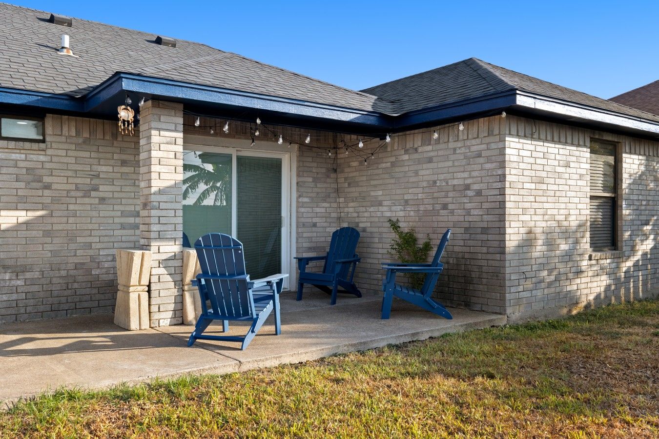 Une maison avec une façade en briques, un patio couvert avec deux fauteuils Adirondack et une porte-fenêtre coulissante.