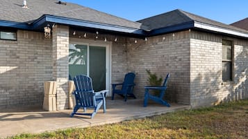 Une maison avec une façade en briques, un patio couvert avec deux fauteuils Adirondack et une porte-fenêtre coulissante.