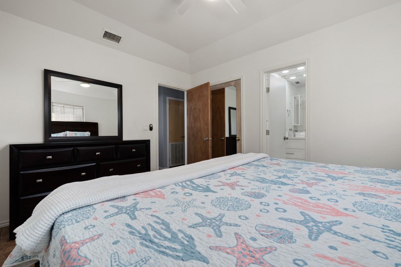 Une chambre à coucher comprenant un lit, une commode, un miroir et une porte donnant sur une autre pièce.
