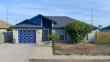 Une maison de plain-pied avec une porte de garage bleue, un petit jardin devant la maison agrémenté d’un palmier, et une clôture en bois.