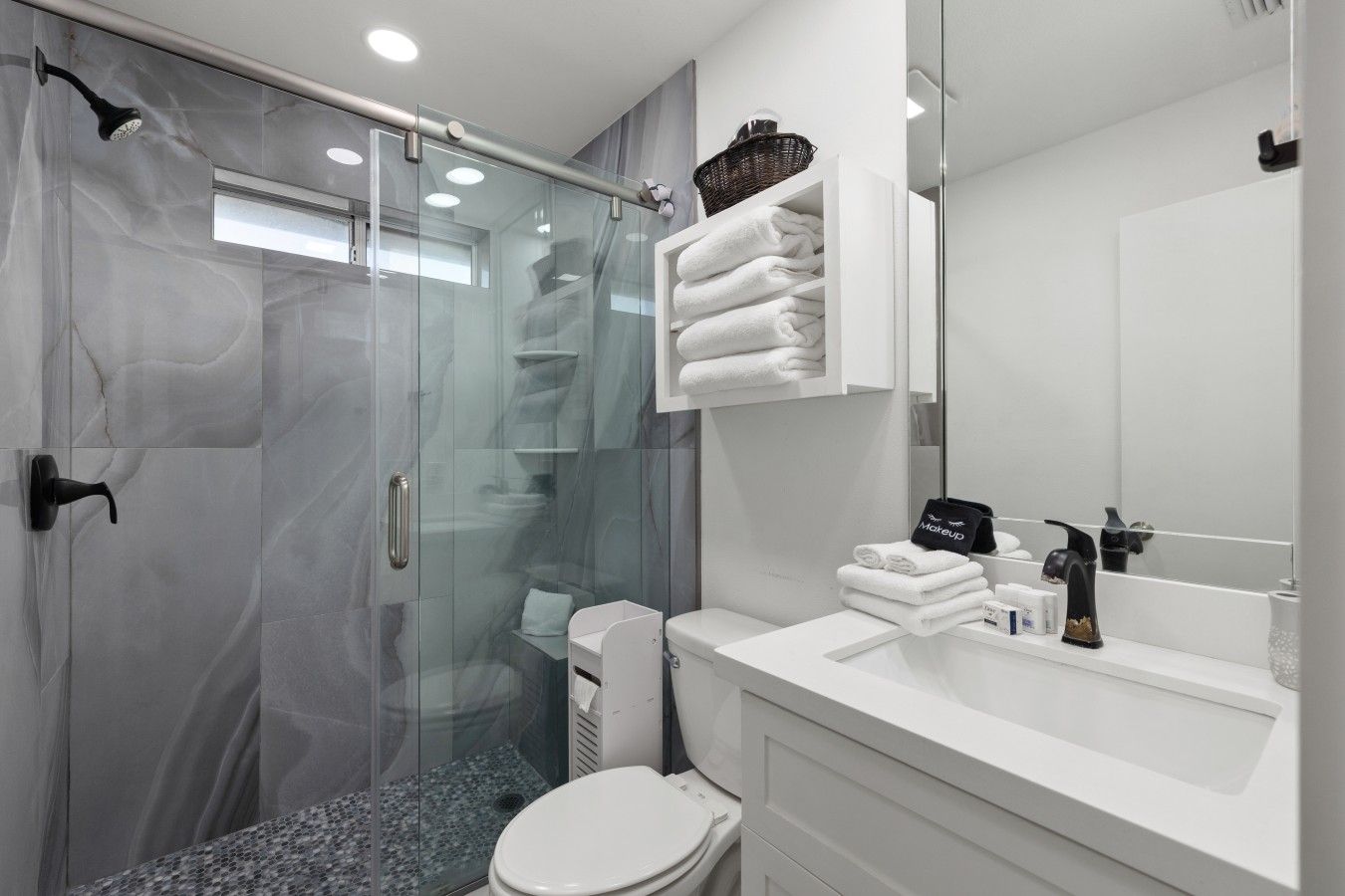A modern bathroom with a glass shower enclosure, a white toilet, and a vanity with a mirror and towel rack.