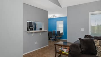 Een woonkamer met een donkerbruine bank, een bijzettafeltje met boeken, een klein plankje met een spiegel en een blauwe muur.