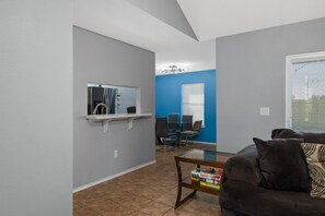 A living room with a dark brown sofa, a coffee table with books, a small shelf with a mirror, and a blue wall. - Cute 2 bedroom home in port Isabel with backyard (Port Isabel)