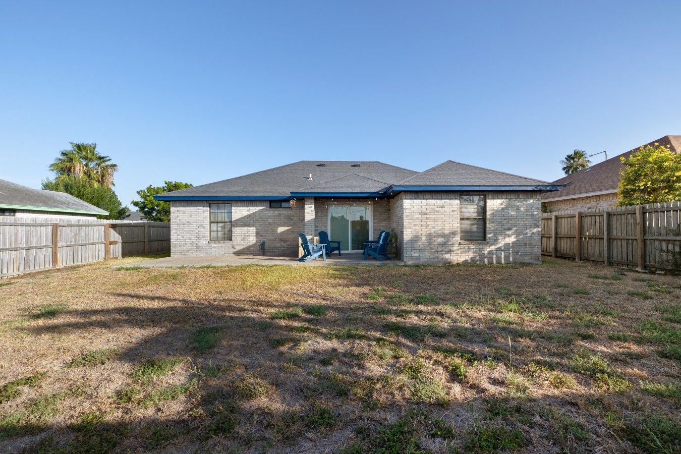 A residential house with a brick exterior, a covered patio, and a fenced backyard.