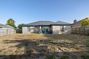 A residential house with a brick exterior, a covered patio, and a fenced backyard.