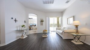 A spacious living area with a glass coffee table, a sofa, and a lamp. There is a doorway leading to another room. - 5BR Tuscan Hills Villa Pool & Themed Rooms (Davenport)