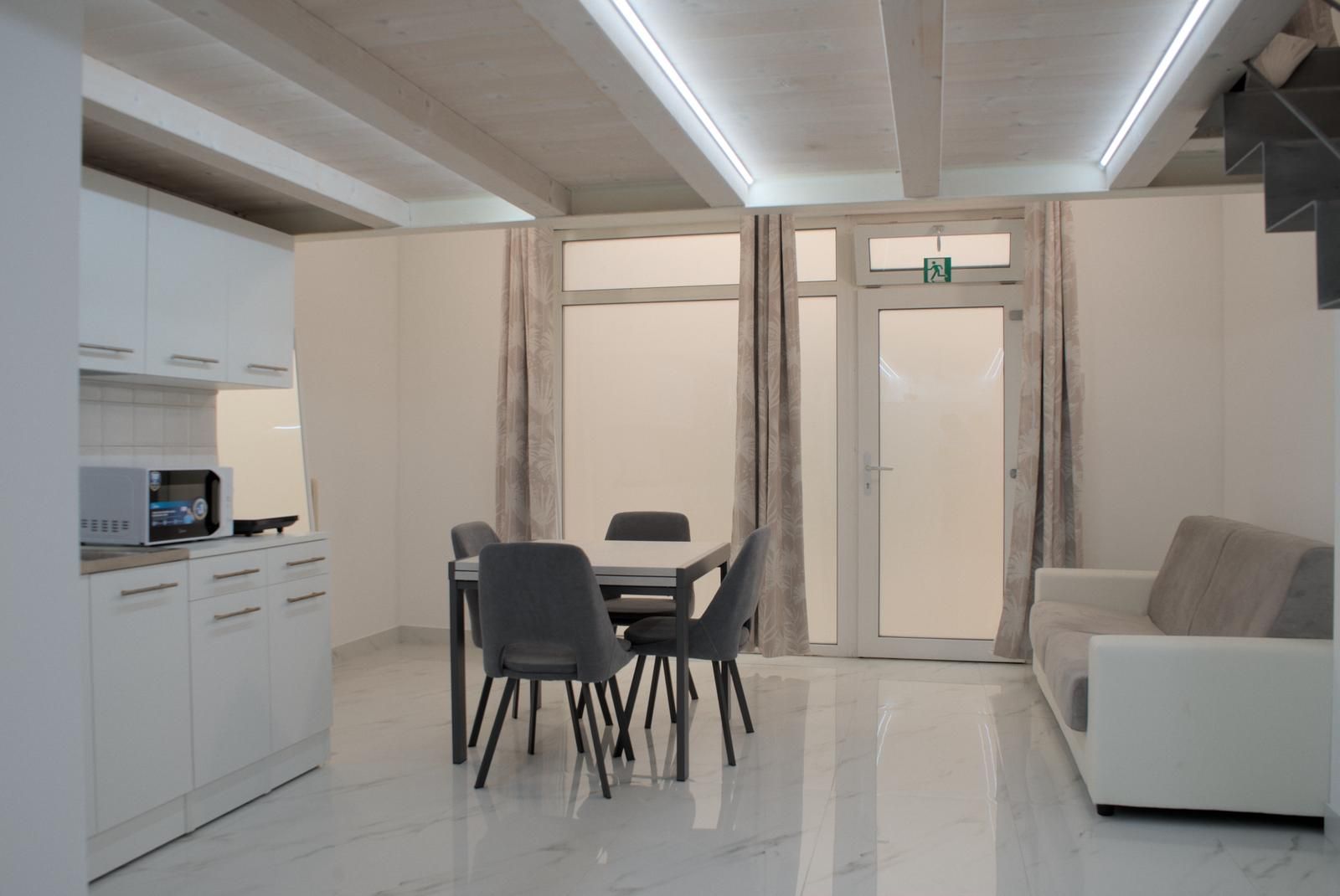 Eine moderne Küche mit Schränken und einer Mikrowelle, ein Essbereich mit Tisch und Stühlen sowie eine Sitzecke mit einer Couch.