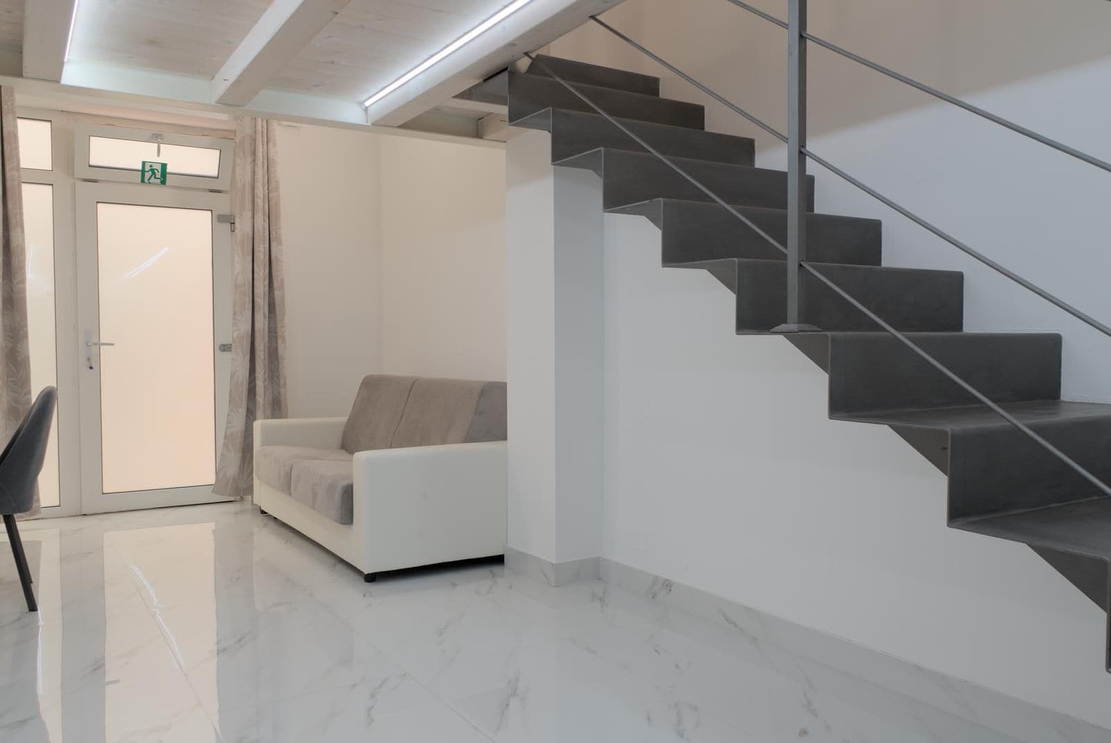 Ein modernes Interieur mit einer Treppe, einem weißen Sofa und einer Tür mit einem Notausgangsschild.