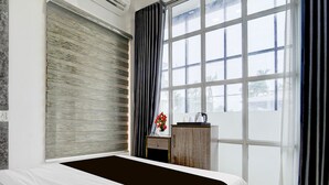 Een moderne slaapkamer met een groot bed, een houten nachtkastje, een klein tafeltje met een bloevas en uitzicht op het omliggende landschap door een groot raam.