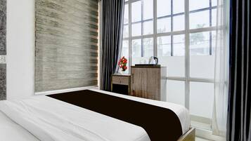 A modern bedroom with a large bed, a wooden nightstand, a small table with a vase of flowers, and a view of the outdoors through a large window.