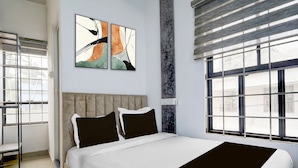Een moderne slaapkamer met een groot bed, twee kunstwerken aan de muur, een raam met zonwering en uitzicht op het omliggende landschap.