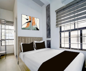 A modern bedroom with a large bed, two wall-mounted artworks, a window with blinds, and a view of the outside. - Classic 1 Botique Hotel (Kanayannur)