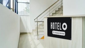 Een hotel receptie met een trap die naar de bovenverdiepingen leidt, een bord met de tekst 'HOTEL & Company-Serviced' en een uitzicht naar buiten door een glazen deur.