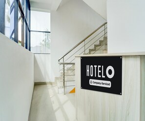 A hotel reception area with a staircase leading to upper floors, a sign indicating 'HOTEL & Company-Serviced', and a view of the outside through a glass door. - Classic 1 Botique Hotel (Kanayannur)
