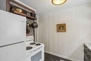 A kitchen with a white refrigerator, a stove, and a wooden shelf above the stove. - Broad Ripple Retreat | Stylish 3BR + Walkable (Indianapolis)