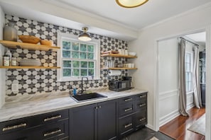 A kitchen with a black and white patterned backsplash, a window, and built-in cabinets with gold handles. - Broad Ripple Retreat | Stylish 3BR + Walkable (Indianapolis)