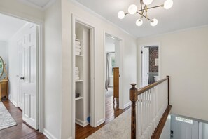 A hallway with a white door, a wooden floor, and a staircase with a white railing. - Broad Ripple Retreat | Stylish 3BR + Walkable (Indianapolis)
