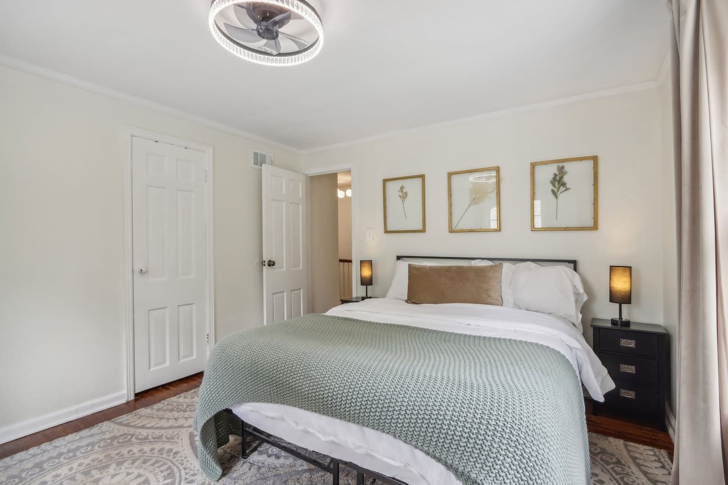 A bedroom with a bed, bedside tables, a ceiling fan, and framed artwork on the wall.