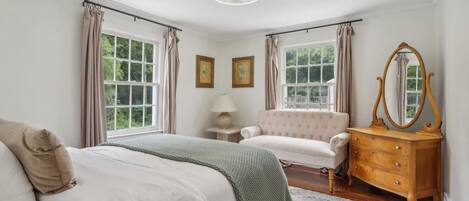 Une chambre à coucher avec un lit, une commode, une chaise et une fenêtre avec des rideaux.