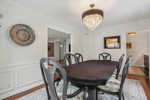 A dining room with a large table, chairs, a chandelier, and a decorative wall piece. - Broad Ripple Retreat | Stylish 3BR + Walkable (Indianapolis)