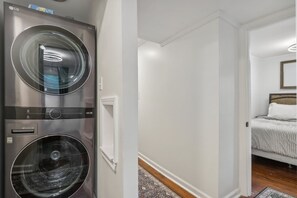 A laundry room with two LG washing machines and a bedroom with a bed and a nightstand. - Modern Broad Ripple Home | 4BR/3 BA | Walkable (Indianapolis)