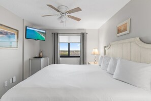 A hotel room with a bed, a ceiling fan, a television, a window with curtains, a bedside lamp, and a framed picture on the wall. - 🌊 Enjoy Stunning Gulf Views | Fabulous Amenities | SunDestin 1803🌊 (Destin)