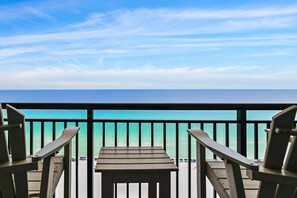 A balcony with two chairs and a small table, overlooking a beach with clear turquoise water and a calm sea under a blue sky. - 🌊 Enjoy Stunning Gulf Views | Fabulous Amenities | SunDestin 1803🌊 (Destin)