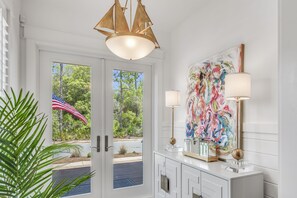 Ein modernes Interieur mit einem großen, abstrakten Gemälde, einer Kristallleuchter und Blick auf einen Garten durch Glastüren.