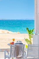 Un balcón con una mesa, una silla y un vaso de zumo de naranja, con vista a una playa y al mar.