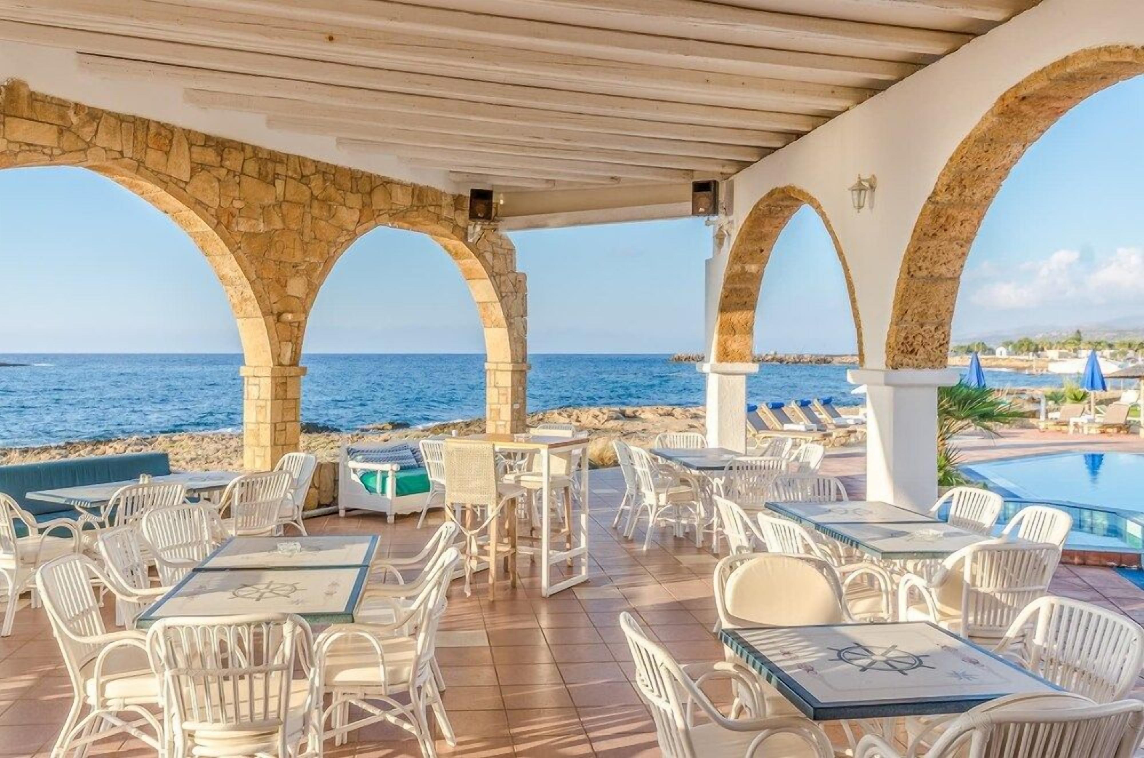 Un área de estar al aire libre con arcos de piedra, mesas y sillas con vistas al mar.