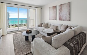 A modern living room with a sofa, a coffee table, and a view of the beach through large sliding doors. - ⛱️Walk to Beach | Gulf Views | Kids Fountain | 2 Pools | Ariel Dunes I 1203☀️ (Miramar Beach)