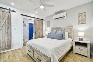 Ein Schlafzimmer mit einem Bett, Nachttischen, einem Deckenventilator, einer Klimaanlage und einer blauen Tür.