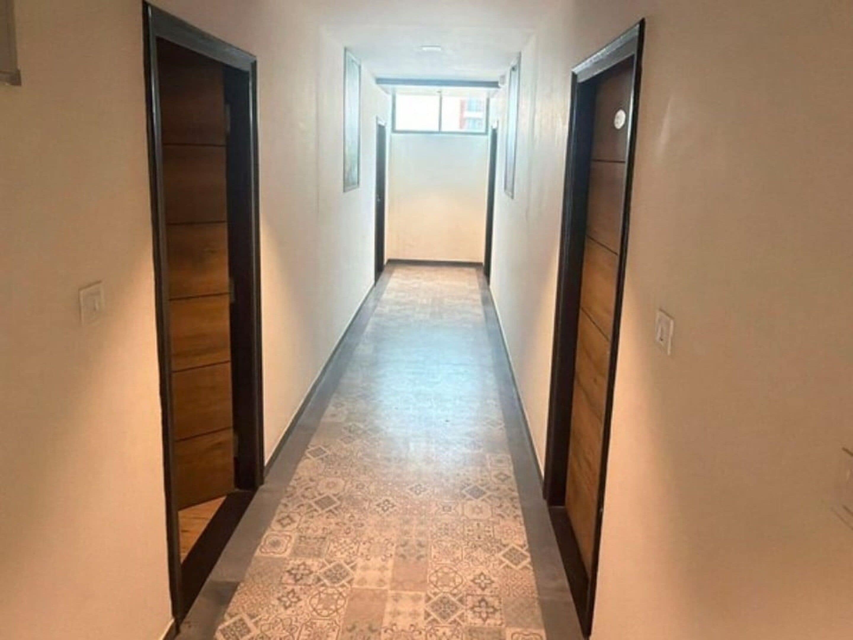 A narrow hallway with patterned flooring and wooden doors on both sides.