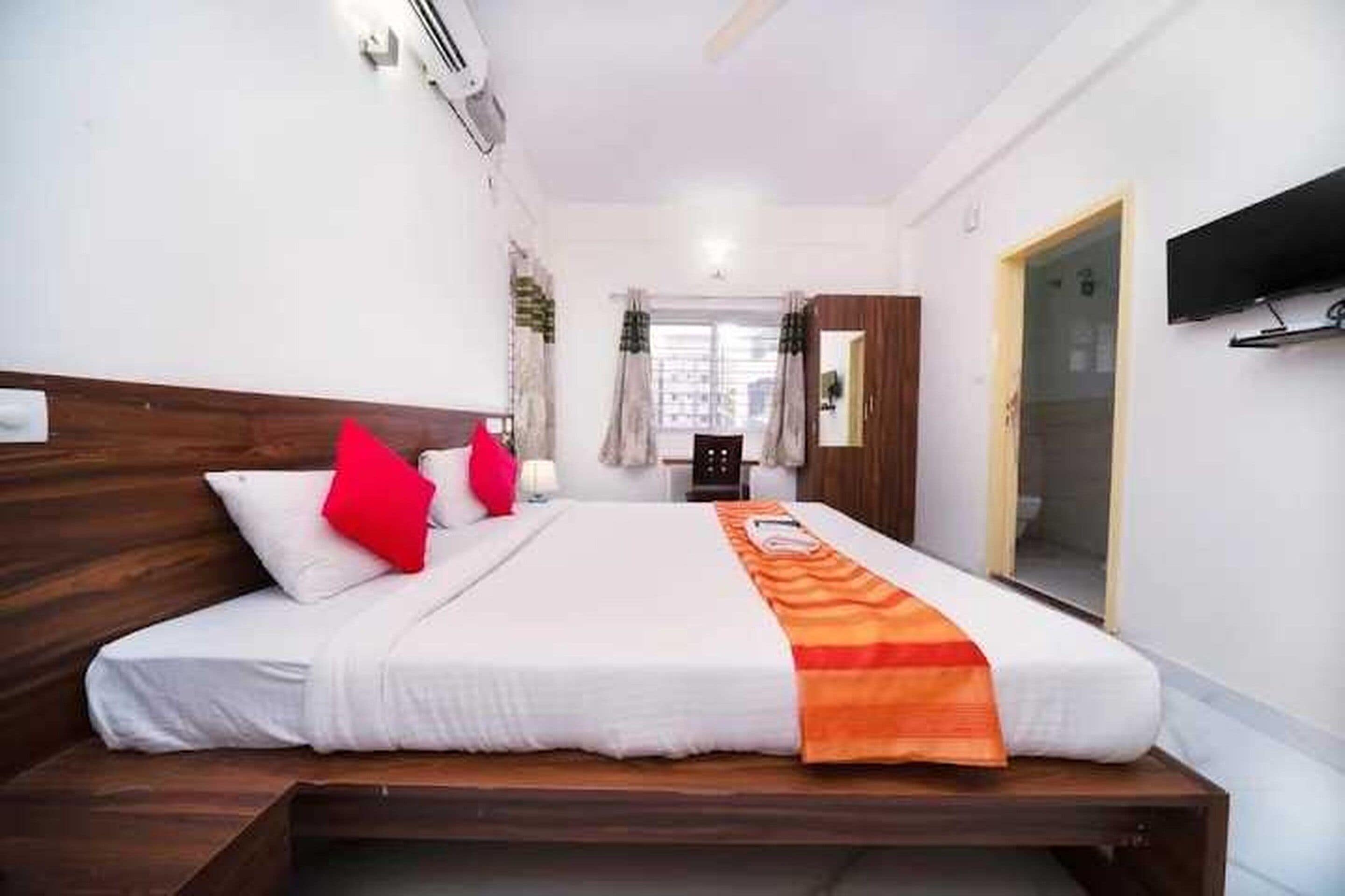 A hotel room with a bed, a TV mounted on the wall, and a window with curtains.