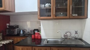 Cozinha com armários de madeira, bancada preta, pia e diversos eletrodomésticos.