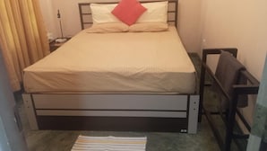 Uma cama de solteiro com cabeceira, um travesseiro vermelho e um tapete listrado no chão.