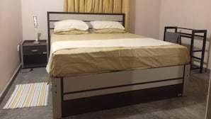 Uma cama de solteiro com cabeceira, mesa de cabeceira e luminária.