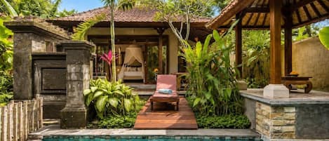Un área de piscina con una tumbona, una pérgola y exuberante vegetación tropical.