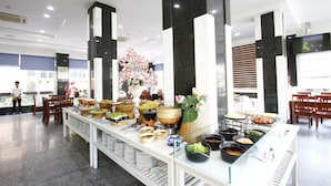 A buffet setup with various food items and a floral centerpiece in a modern hotel setting. - Song Cong Hotel Danang (Da Nang Municipality)