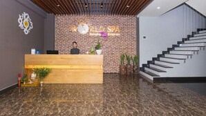 A reception desk with a wooden counter, a brick wall with a logo, and a staircase. - Song Cong Hotel Danang (Da Nang Municipality)