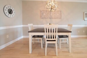 A dining room with a wooden table and chairs, a wall clock, and a decorative light fixture. - Folly Road Retreat - Folly Beach Monthly Rental (Folly Beach)
