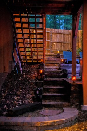 A set of outdoor wooden steps leading to a covered area with a metal gate, surrounded by a wooden fence and a small garden area with steps and a lantern. - Stylish Zen Mountain Villa: Hot Tub, Games & Views (Flagstaff)
