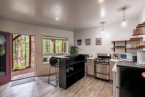 A modern kitchen with a large island, stainless steel appliances, and a view of the forest through the windows. - Stylish Zen Mountain Villa: Hot Tub, Games & Views (Flagstaff)