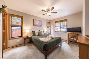 A bedroom with a bed, a ceiling fan, a television, and windows with blinds. - Stylish Zen Mountain Villa: Hot Tub, Games & Views (Flagstaff)