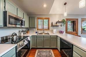 A modern kitchen with green cabinets, stainless steel appliances, and a large window. - Stylish Zen Mountain Villa: Hot Tub, Games & Views (Flagstaff)