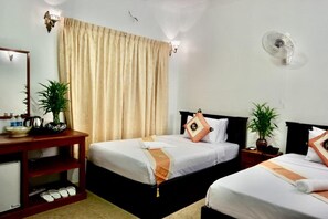 Habitación de hotel con dos camas, una mesita de noche con lámpara, un espejo, un ventilador de pared y una ventana con cortinas.