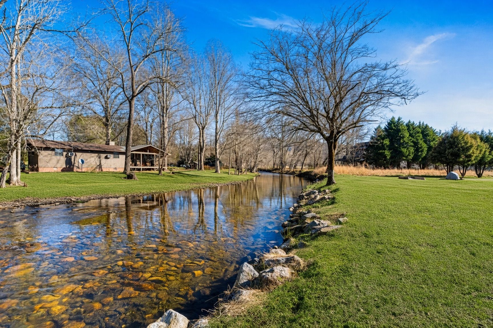 Een pand aan de rivier met een huis, een gazon en bomen.
